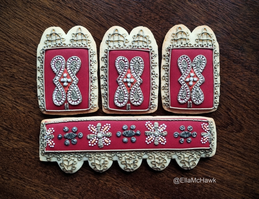 
A set of four biscuits made to look like the decorative cuff of an early modern glove. Each biscuit is iced in the same maroon-red icing and embellished with details that look like pearls, silver-gilt threads, and bobbin lace. The top row features three rectangular biscuits with a diamond-shaped motif at the centre of each one. Below is a single long rectangle decorated with a row of stylised flowers.